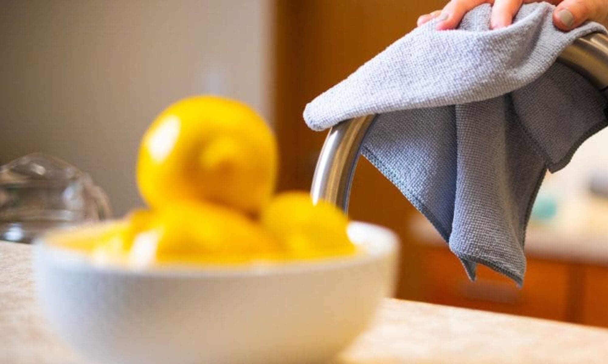 Bowl of lemons and a hand cleaning a faucet