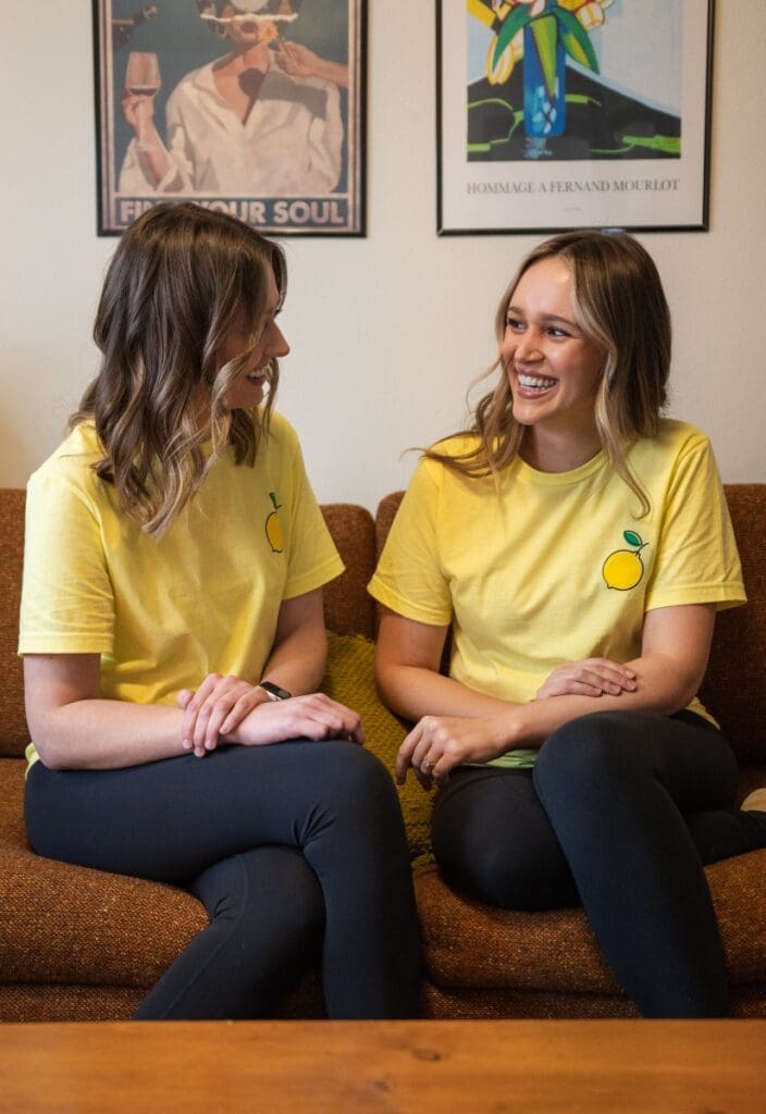Two Lemon Fresh Cleaners owners wearing branded shirts, sitting on a couch and smiling