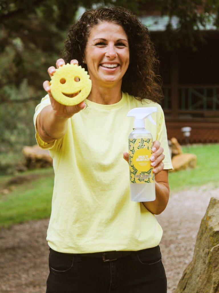 Brean Stiefel holding a cleaning sponge and bottle of multi surface cleaner