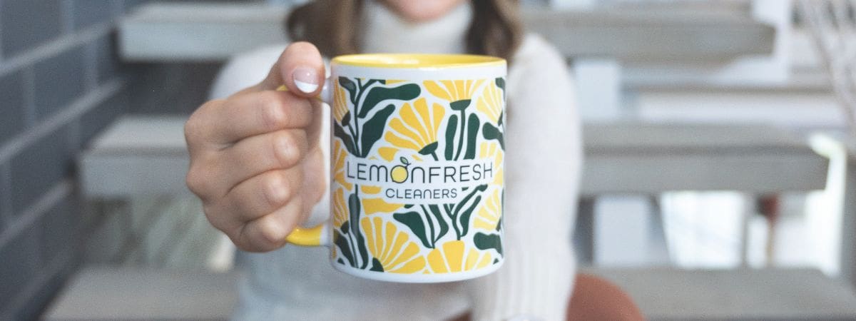 Hand holding a Lemon Fresh Cleaners mug with person in background sitting on indoor stairs